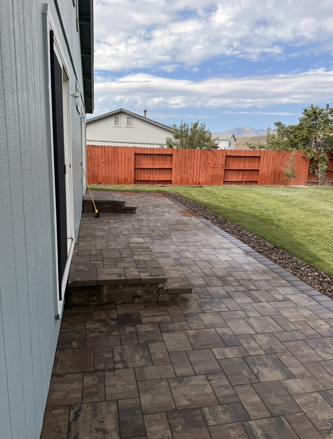 Paver patio with stairs and lush green lawn against red fence